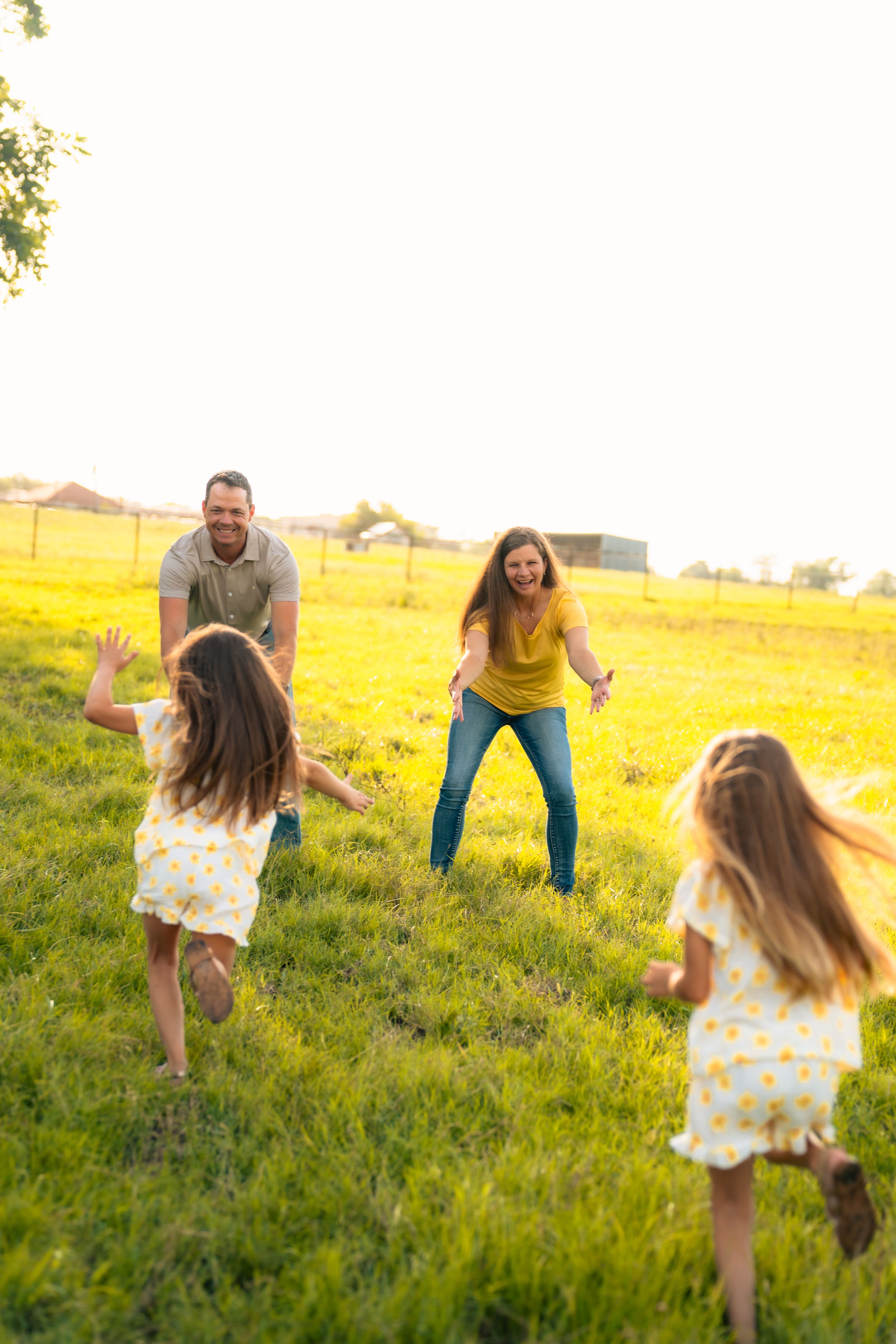 Family runs and plays together in a sunny grassy field during golden hour at sunset.