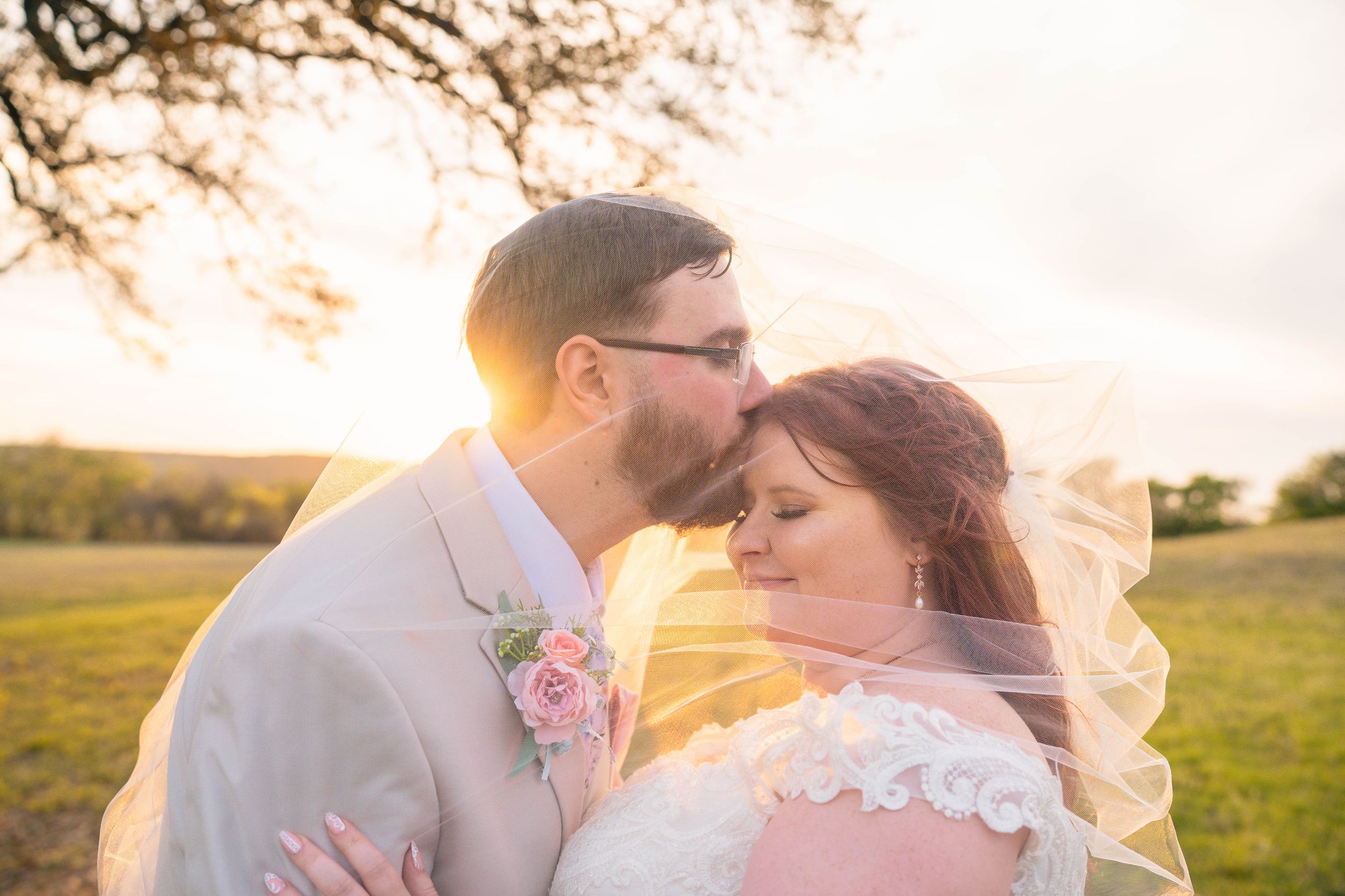 Romantic backlit portrait of newlyweds embracing at sunset in an open field.