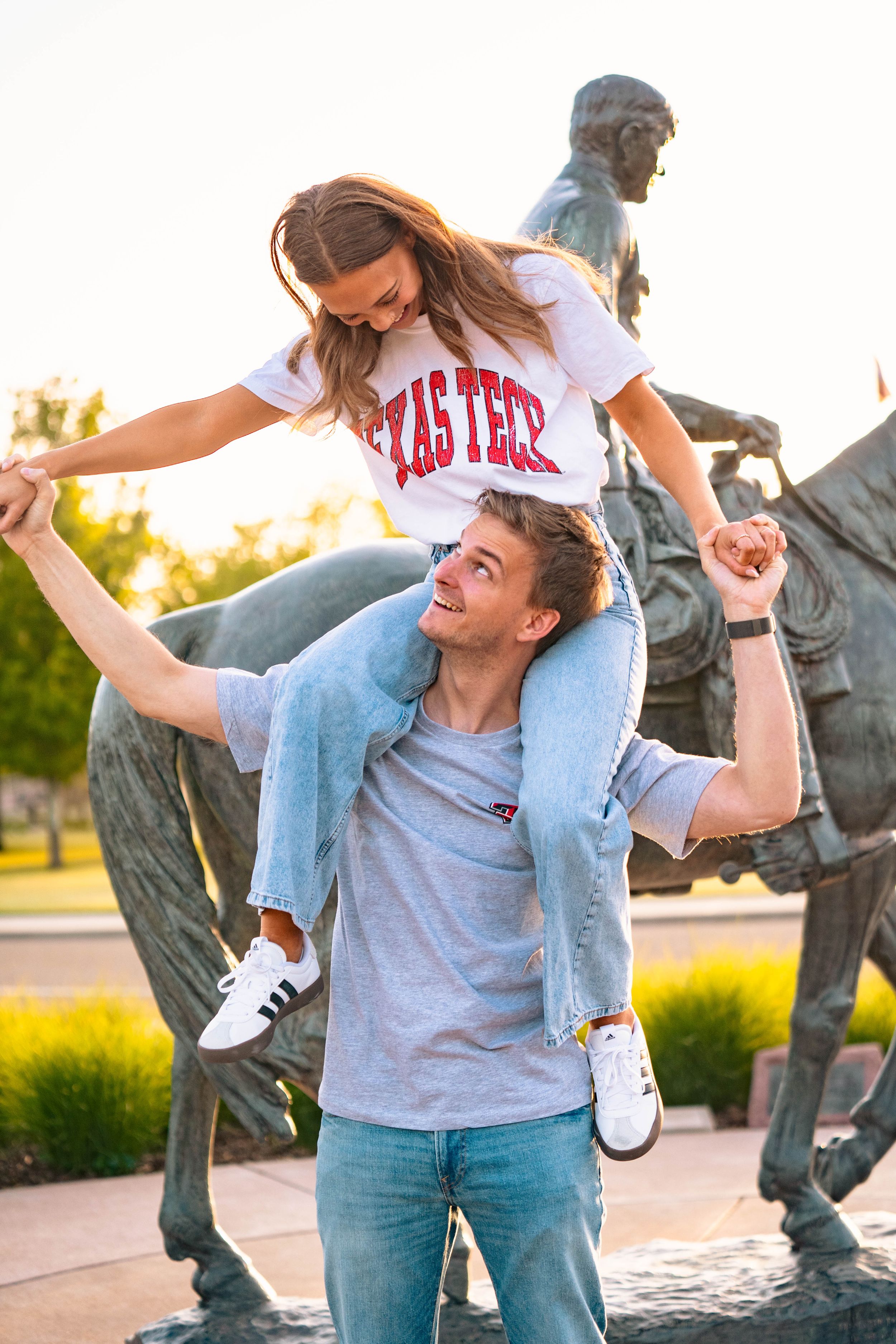 Playful couple having fun near campus statue with piggyback ride.