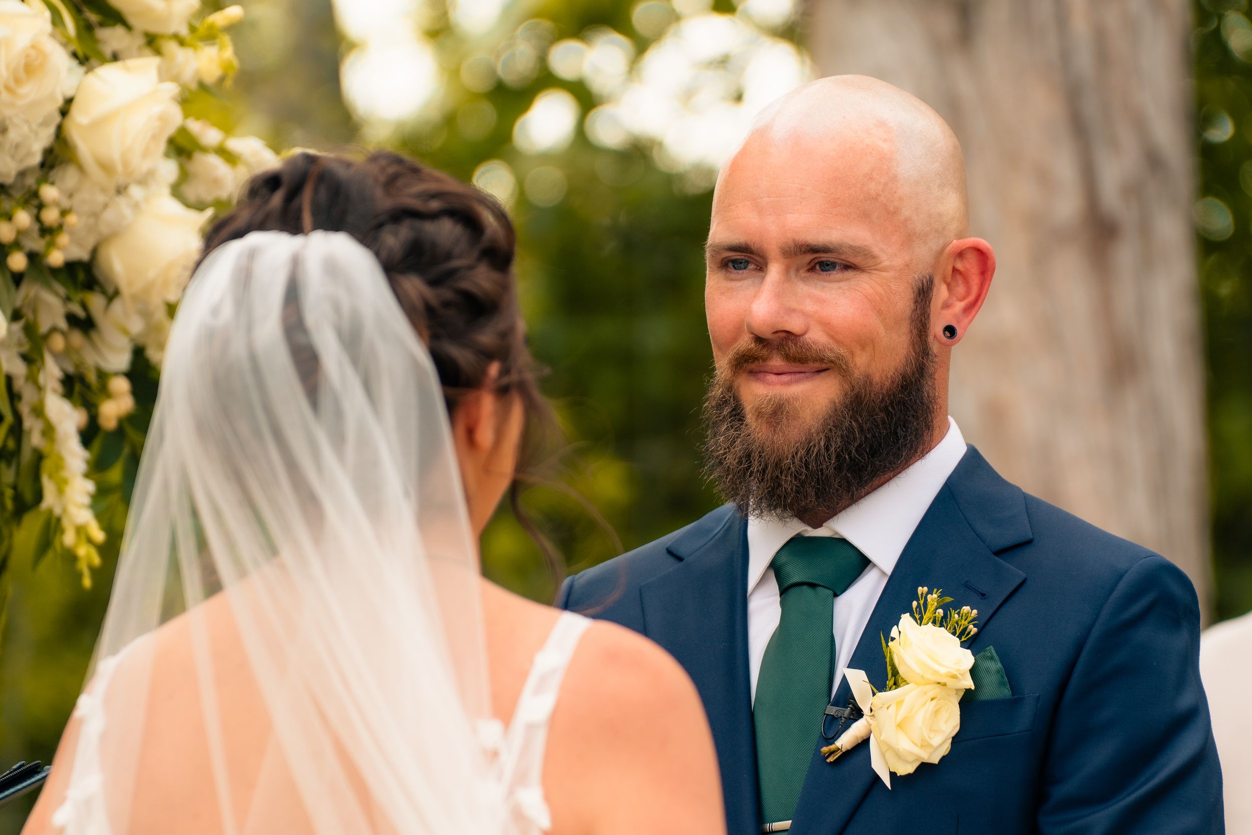 Two people share an intimate moment during an outdoor wedding ceremony under floral decorations.