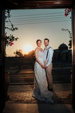 A couple poses for sunset photos on a brick patio with a glowing golden sky in the background.