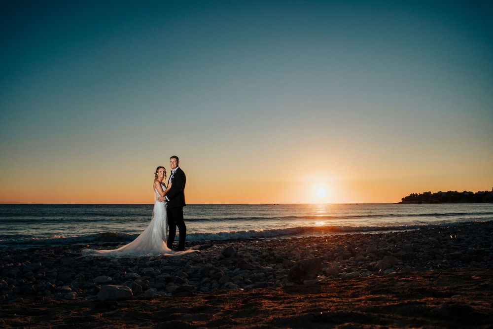 Silhouettes stand together on a beach at sunset with golden light reflecting off the ocean and sand.