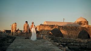 Wedding party walking along ancient stone ruins at sunset with a Mediterranean building in the background.