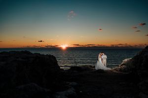 Stunning sunset over the ocean horizon with silhouetted rocks and warm orange sky reflecting on calm waters.