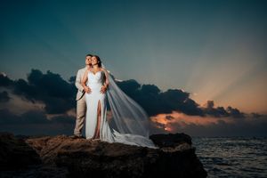 A romantic beach wedding photo session at sunset with a flowing white dress and dramatic sky in the background.