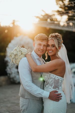 Happy newlyweds embrace and laugh together during golden hour sunset at their outdoor wedding celebration.