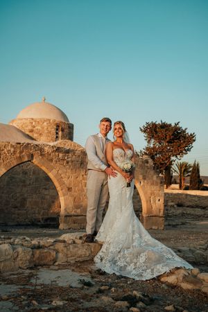 A wedding couple poses at sunset in front of a historic domed stone church in Mediterranean architecture.