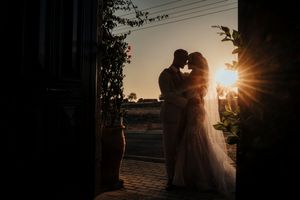 Silhouetted couple embraces during golden sunset with sun rays peeking through trees and power lines.