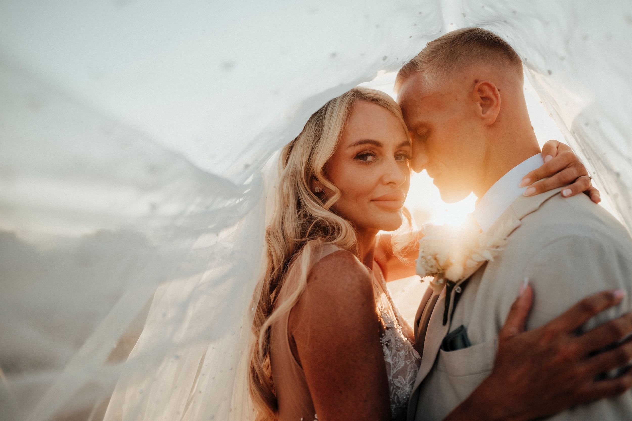 A romantic couple embraces during golden hour sunset while posing for intimate outdoor portrait photos.