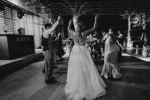 A wedding couple and their guests dance together in a dimly lit reception venue during a celebration.