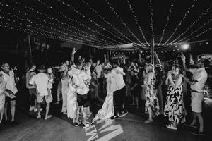 Wedding guests dance under twinkling string lights at an outdoor evening reception celebration.