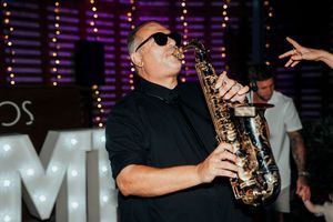 Musicians perform with saxophones and other instruments on stage with illuminated letters visible in background.
