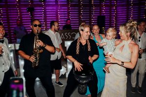 Wedding guests dance together on a dimly lit dance floor with purple lighting in the background.