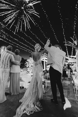 Wedding guests dance and celebrate under sparkling fireworks display at an outdoor nighttime reception.