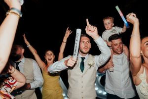 Wedding party guests dancing and celebrating with raised arms on the dance floor at a reception.