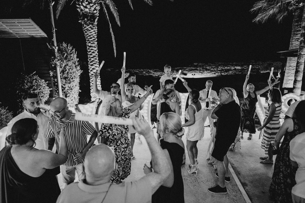 Black and white photo of people dancing at a nighttime outdoor party with palm trees in the background.