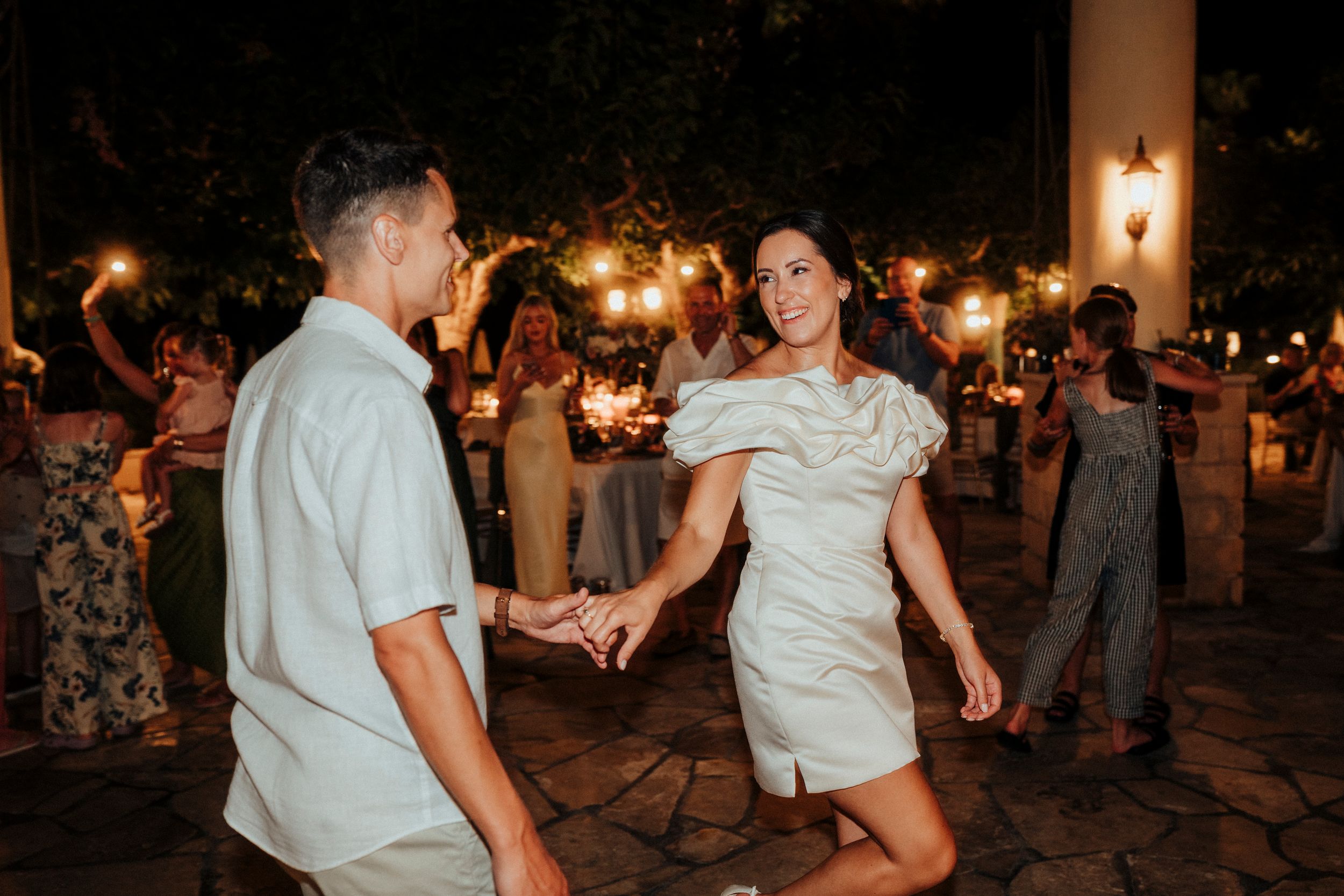 Wedding guests dance and celebrate on an outdoor dance floor during an evening reception with warm lighting.