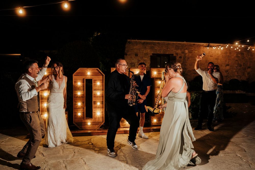 Wedding party dancing and celebrating at a romantic evening reception with warm string lights overhead.