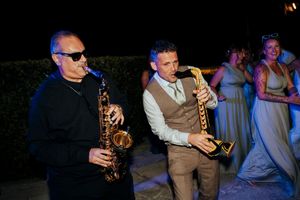 Musicians playing saxophones at an outdoor nighttime wedding reception with ambient lighting.