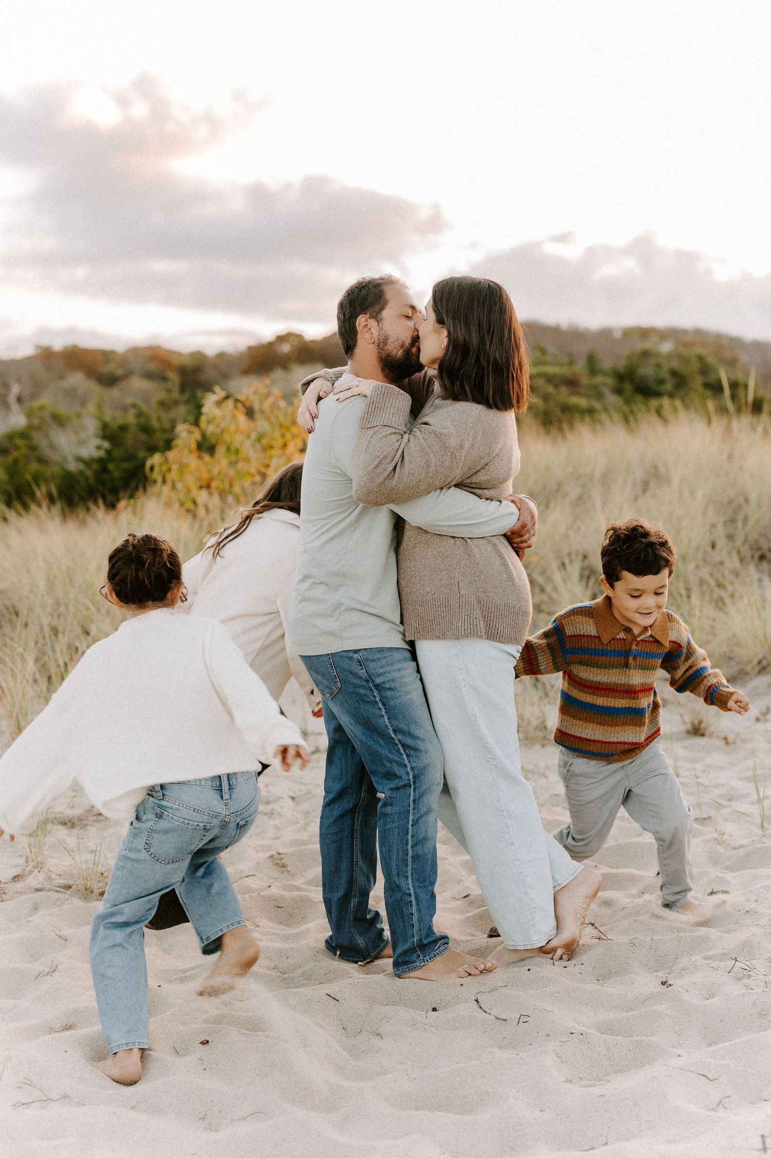 A family plays and runs together on sandy dunes during a sunset photoshoot.