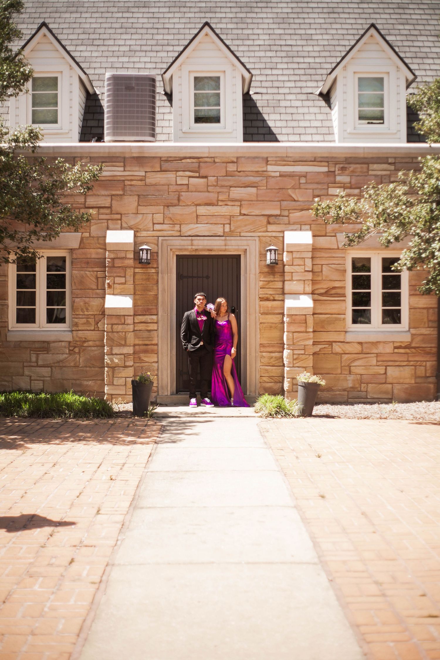 Couple in formal attire posing outside stone mansion on prom night.