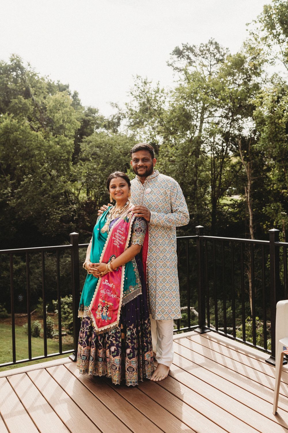 Indian couple in traditional attire posing on a wooden deck surrounded by lush greenery during a wedding celebration in Knoxville, TN.