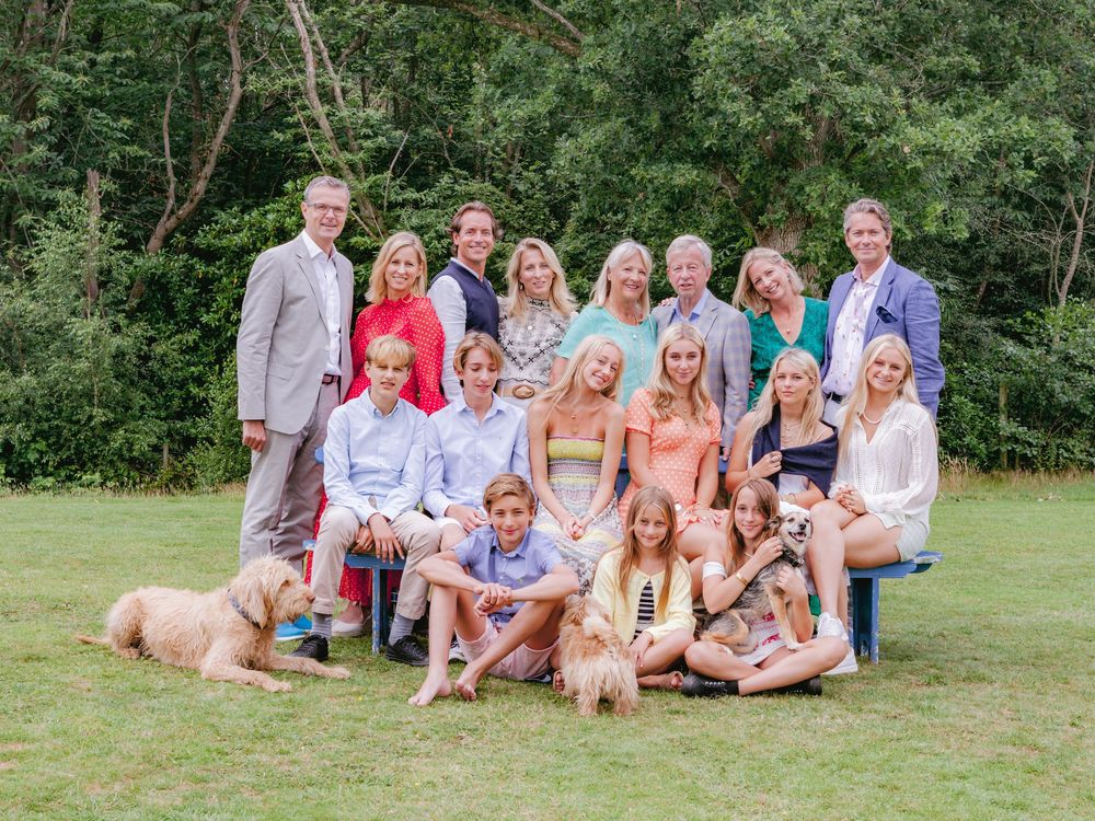 Large family group poses together on grass with two golden retrievers in a summery outdoor setting.
