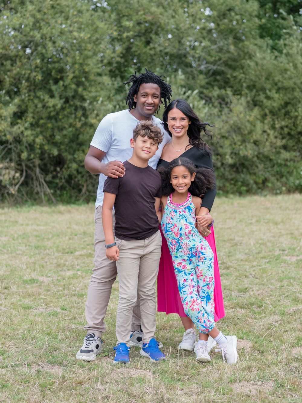 A smiling group poses together outdoors on grassy ground for a casual photo session on a sunny day.