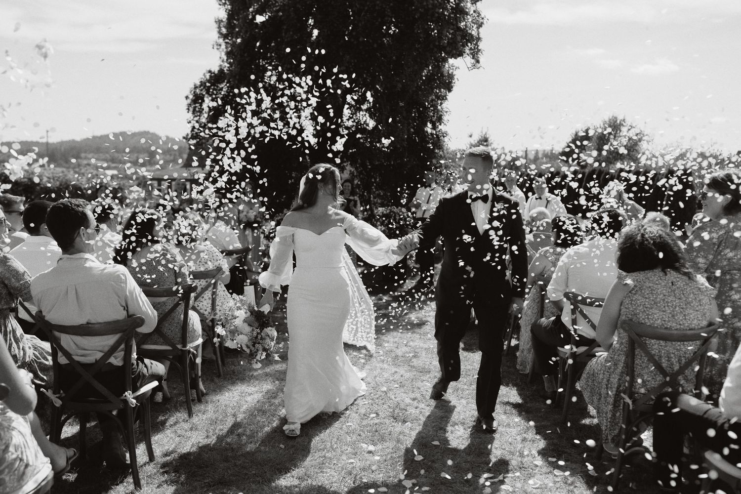 A black and white photo of a wedding ceremony exit with guests throwing confetti.