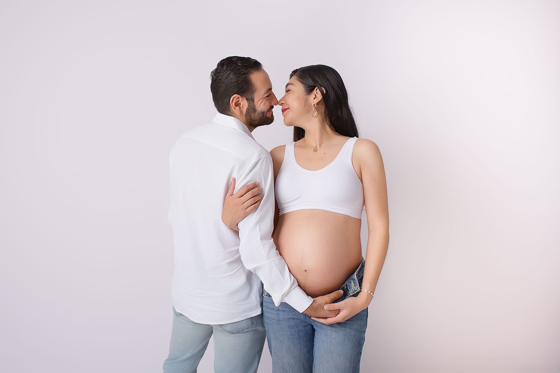 Happy couple expecting a baby, man embracing pregnant woman's belly, sharing a tender moment on white background.