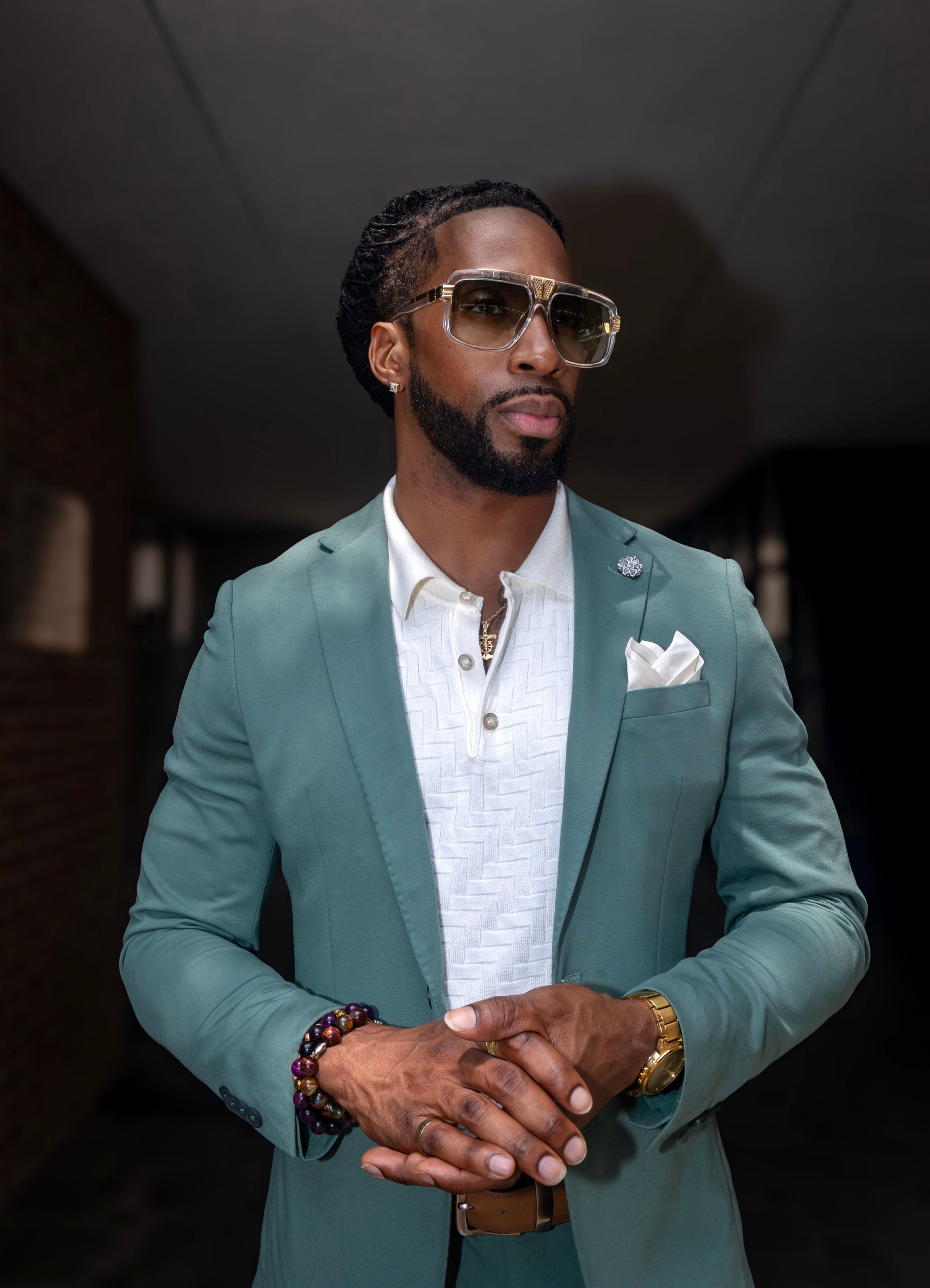 Stylish portrait of person wearing mint green blazer and sunglasses in dark hallway.