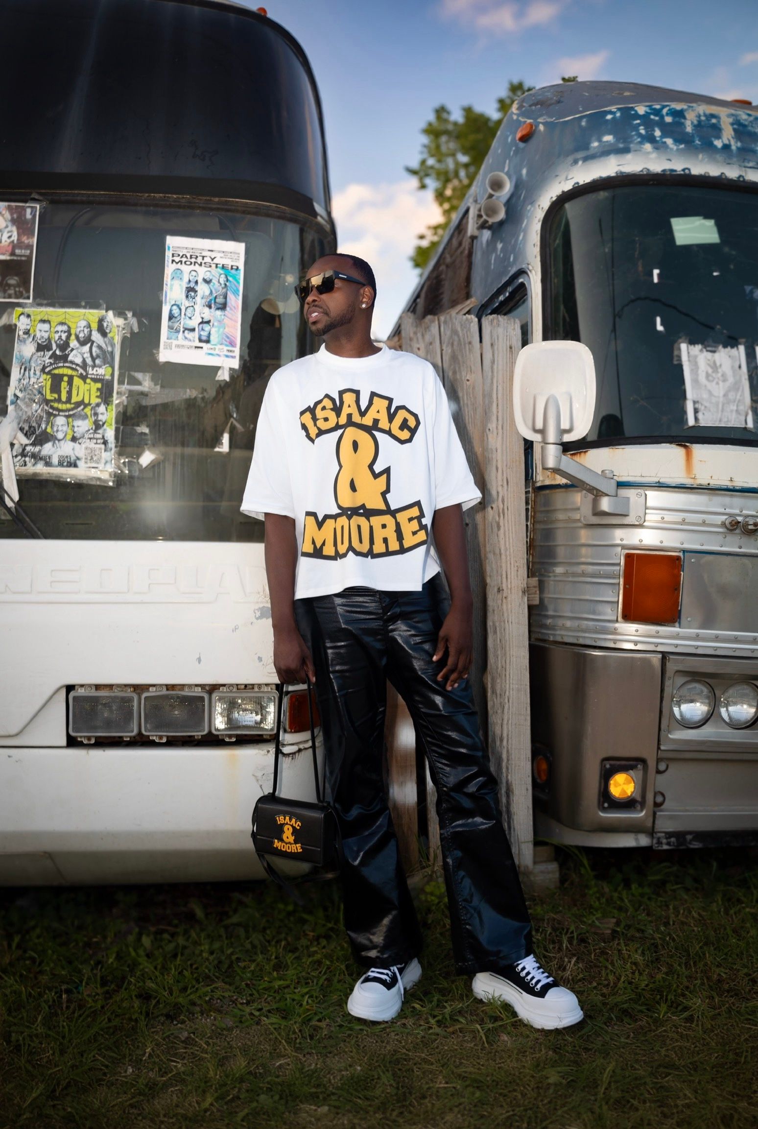 Person wearing white graphic t-shirt standing between two tour buses.