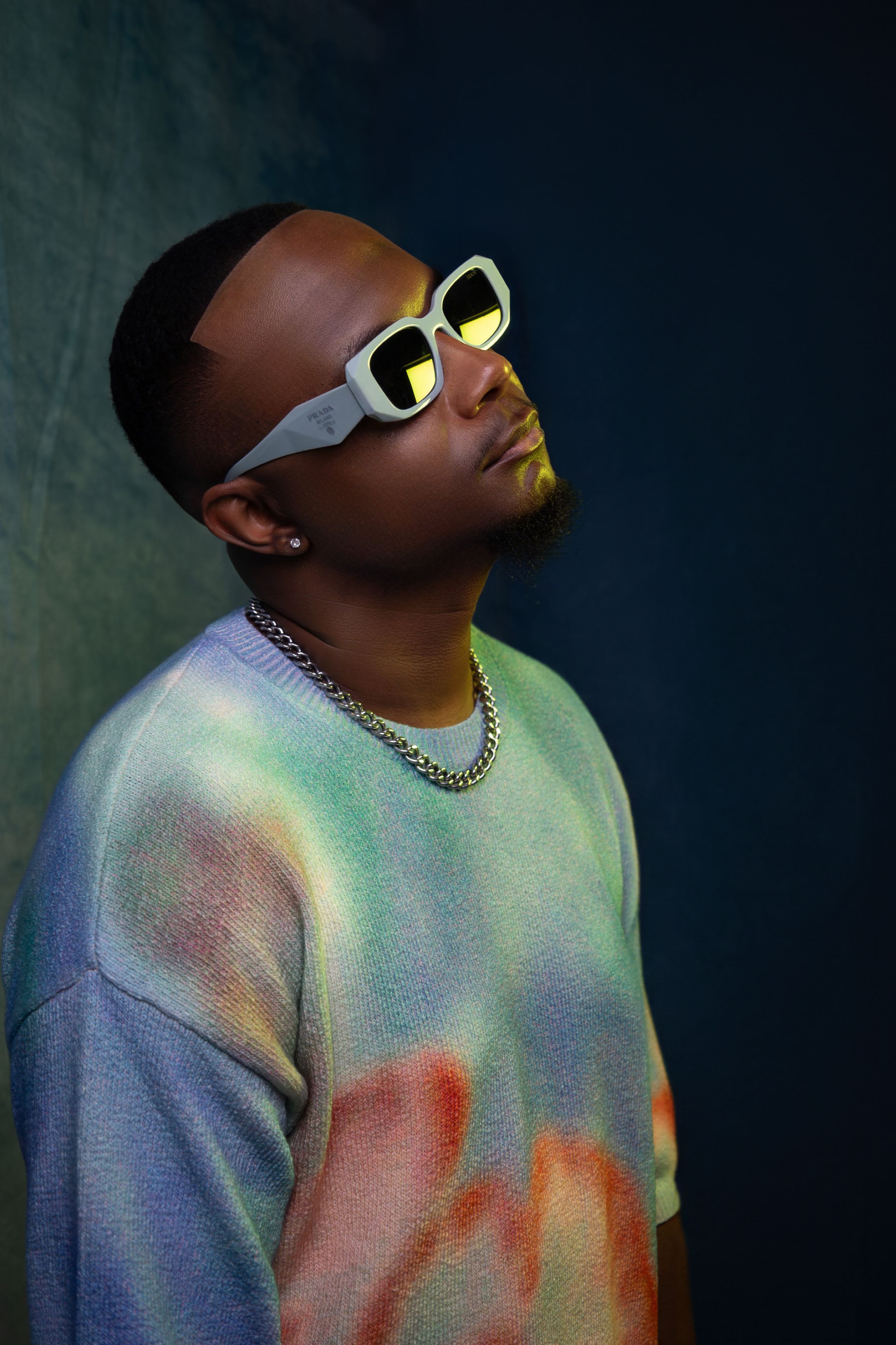 Portrait of person wearing tie-dye sweatshirt and reflective sunglasses against dark background.