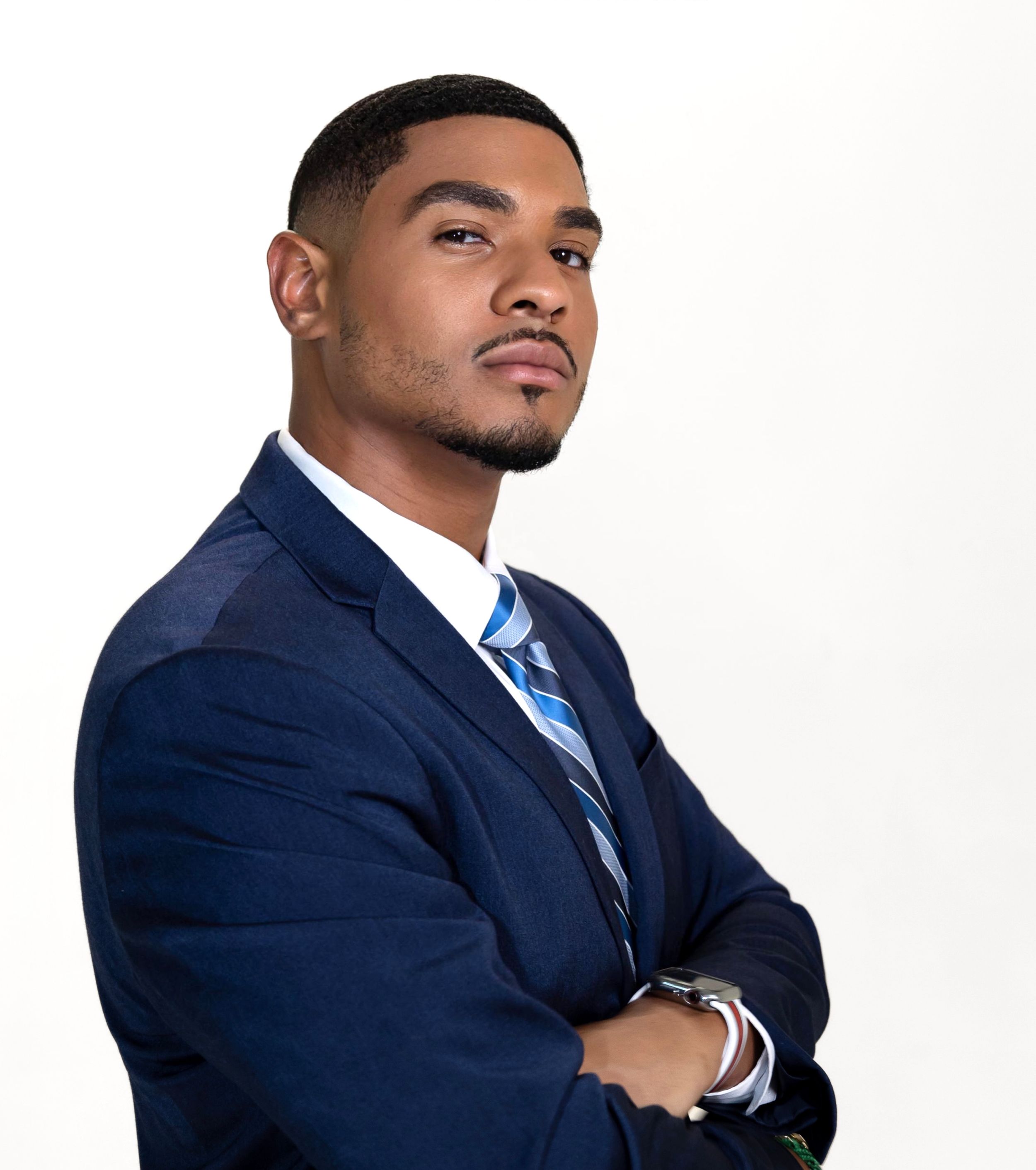Professional headshot of person in navy suit and striped tie against white background.