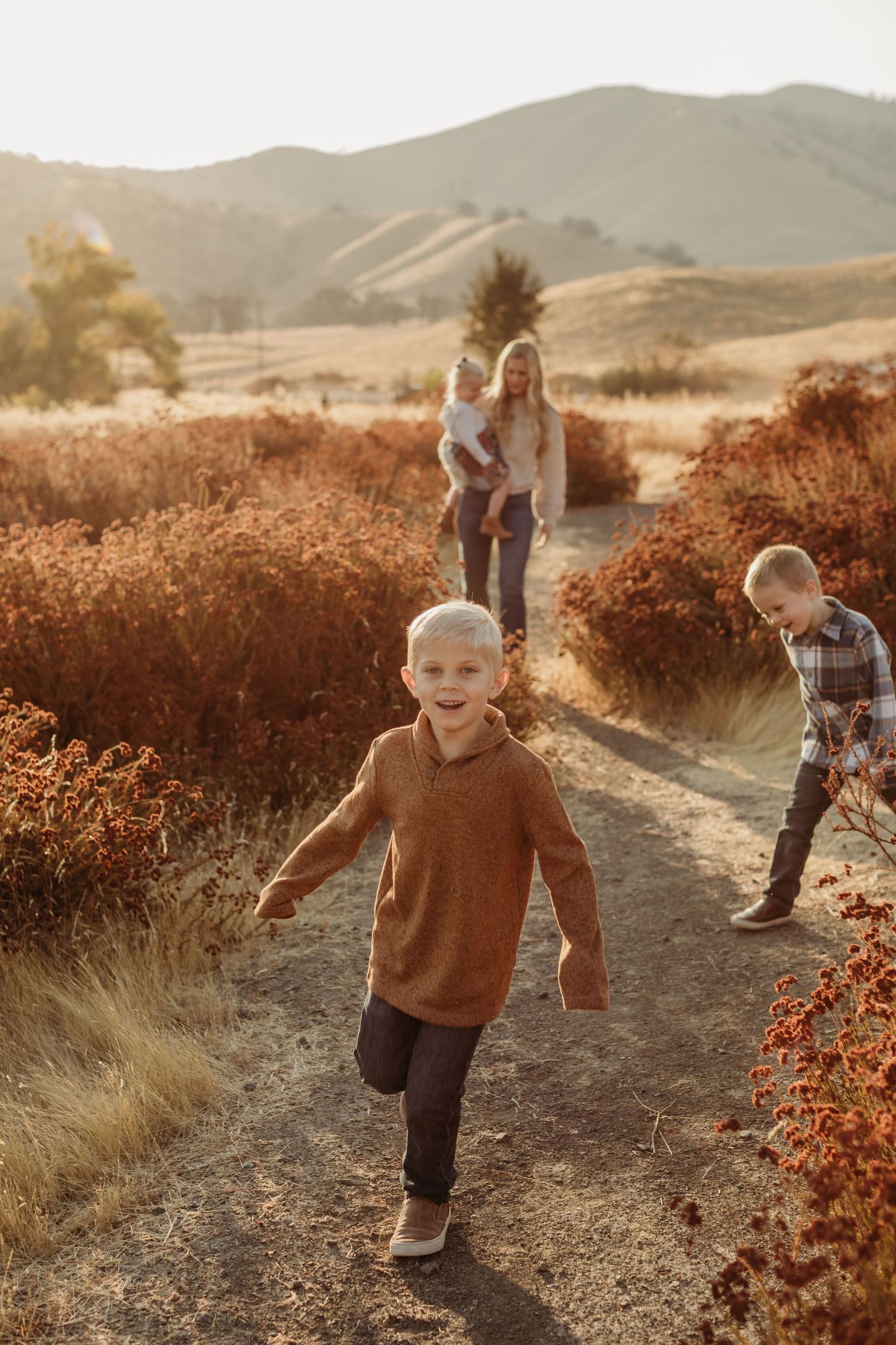 A family walks along a dusty trail through golden brush during sunset in the mountains.