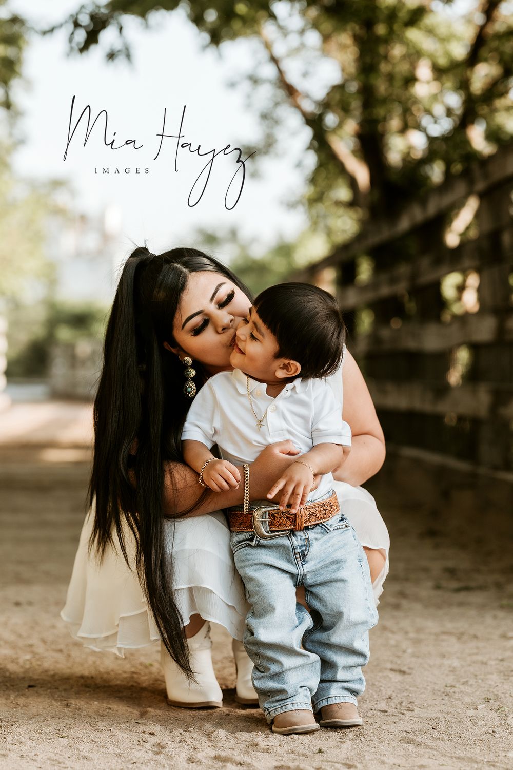 A tender moment between parent and child in casual white and denim outfits against a natural outdoor backdrop.