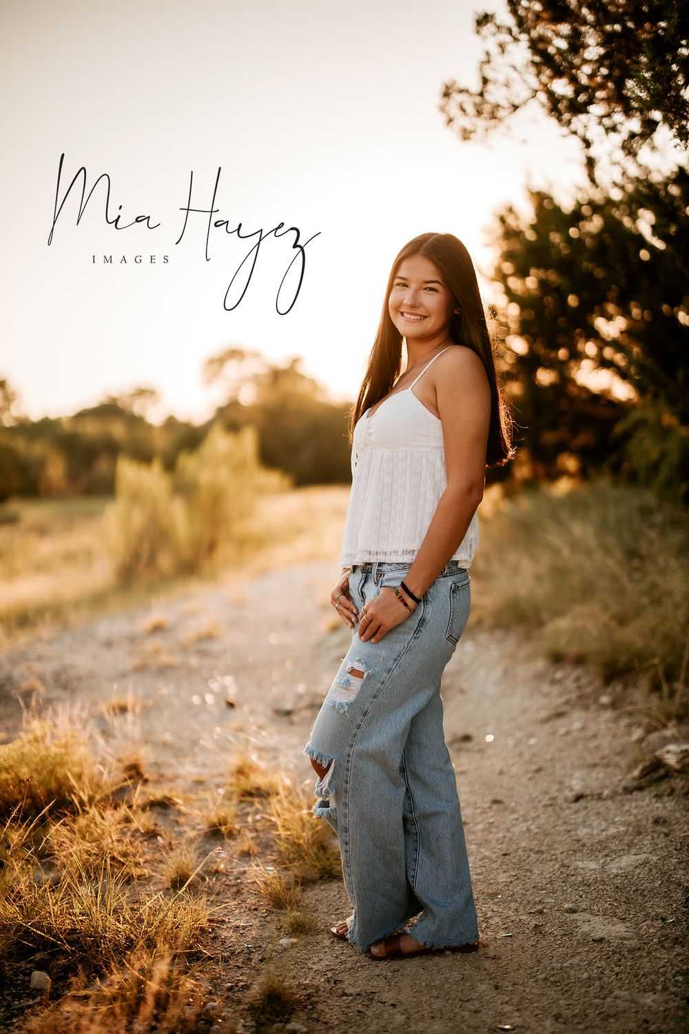 Woman in casual denim poses along nature trail during golden hour sunset photoshoot.