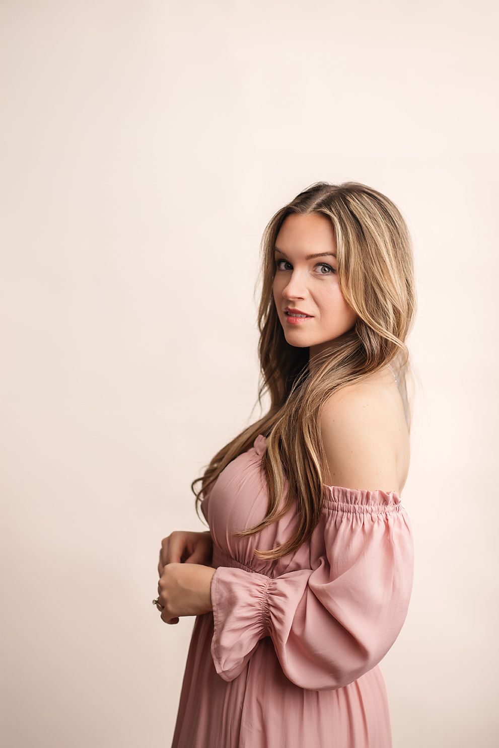 Young woman in white top and pink wide-leg pants posing on pink background.