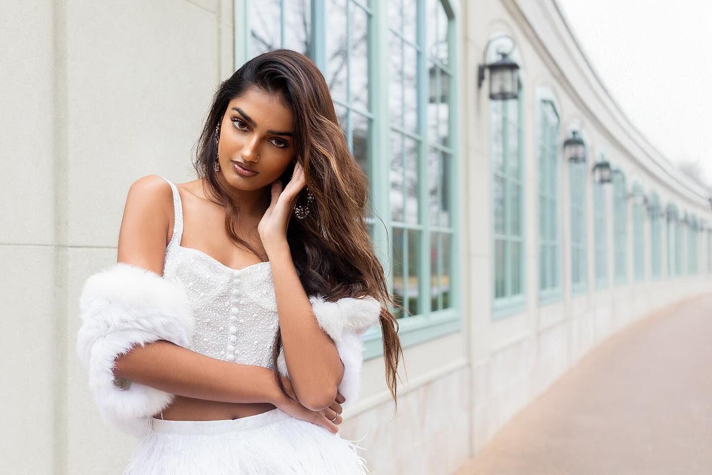 Woman in white dress poses elegantly against modern glass building exterior.