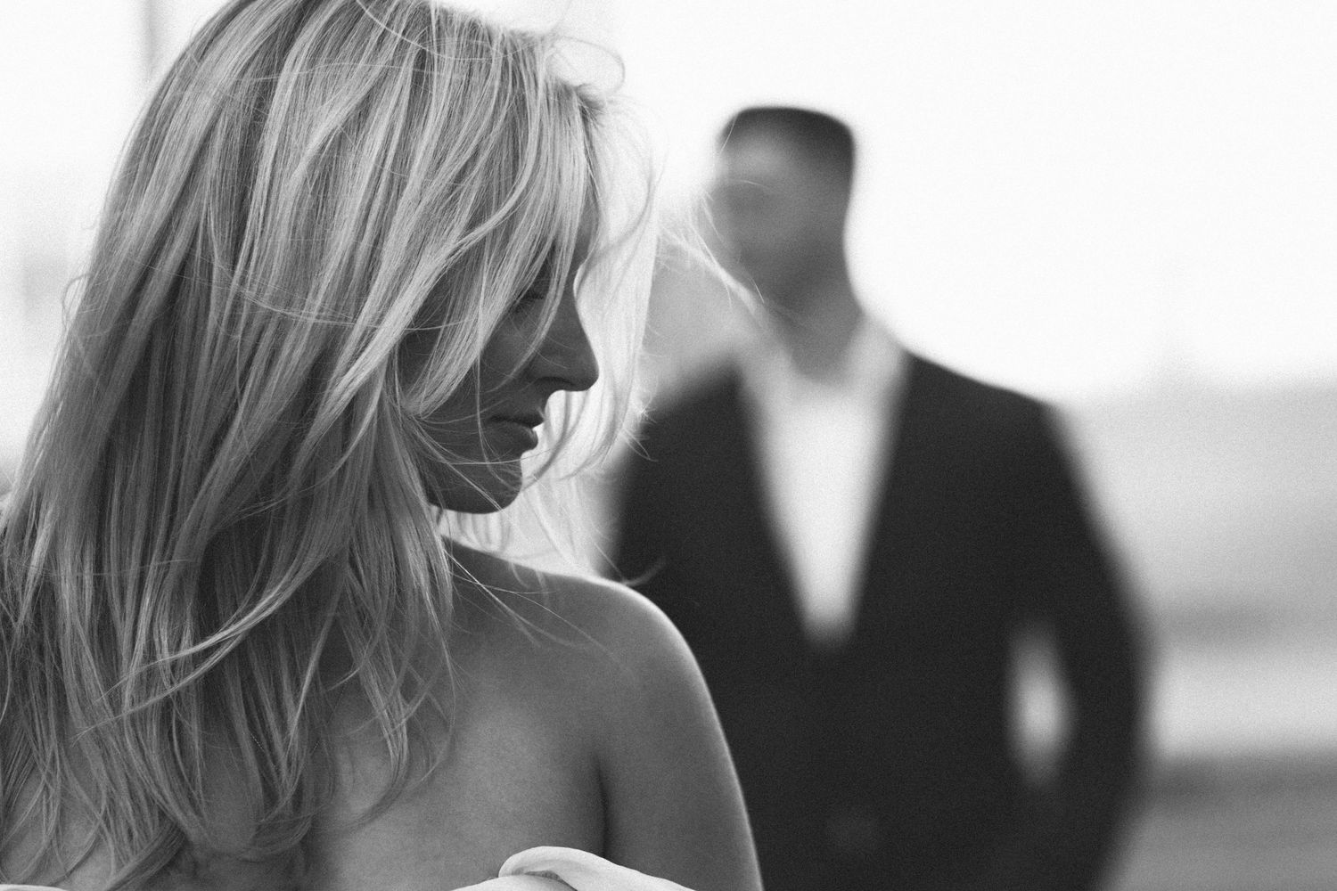 Artistic black and white portrait with woman in foreground and silhouetted figure behind.