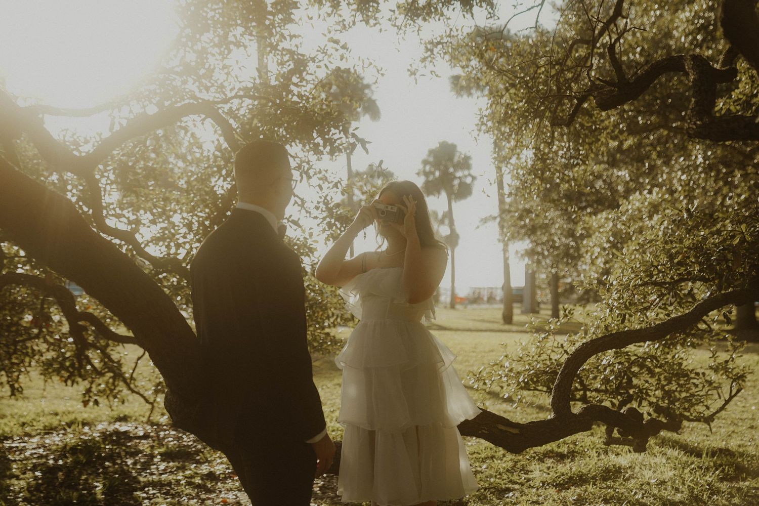 A romantic silhouette of a couple standing by a large tree branch during a golden sunset.