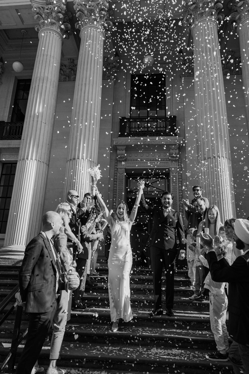 Wedding celebration with confetti falling between classic white columns at a grand building entrance.