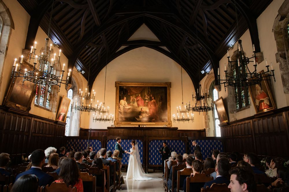 Wedding ceremony in a grand historic hall with chandeliers and wooden beams.