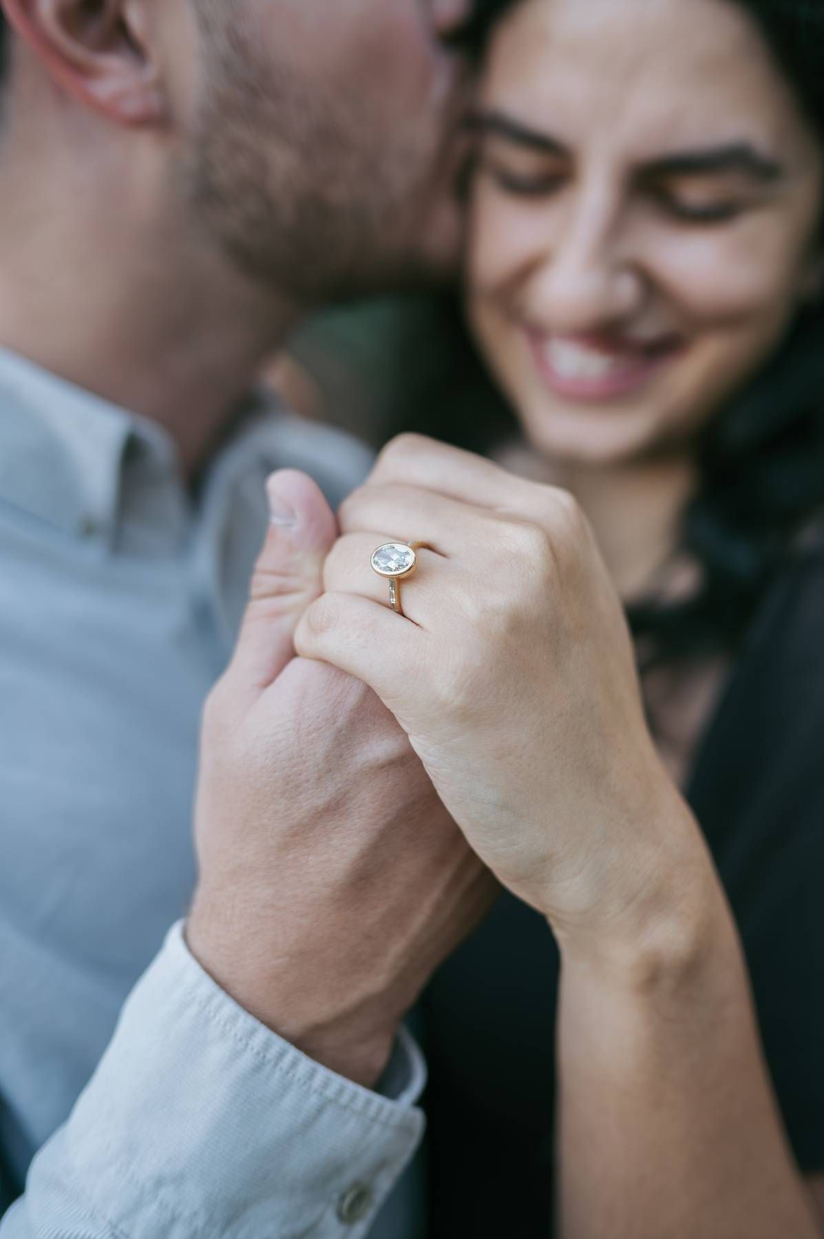 Close-up of engagement ring on woman's hand as man kisses her cheek, engagement photographer Greensboro NC