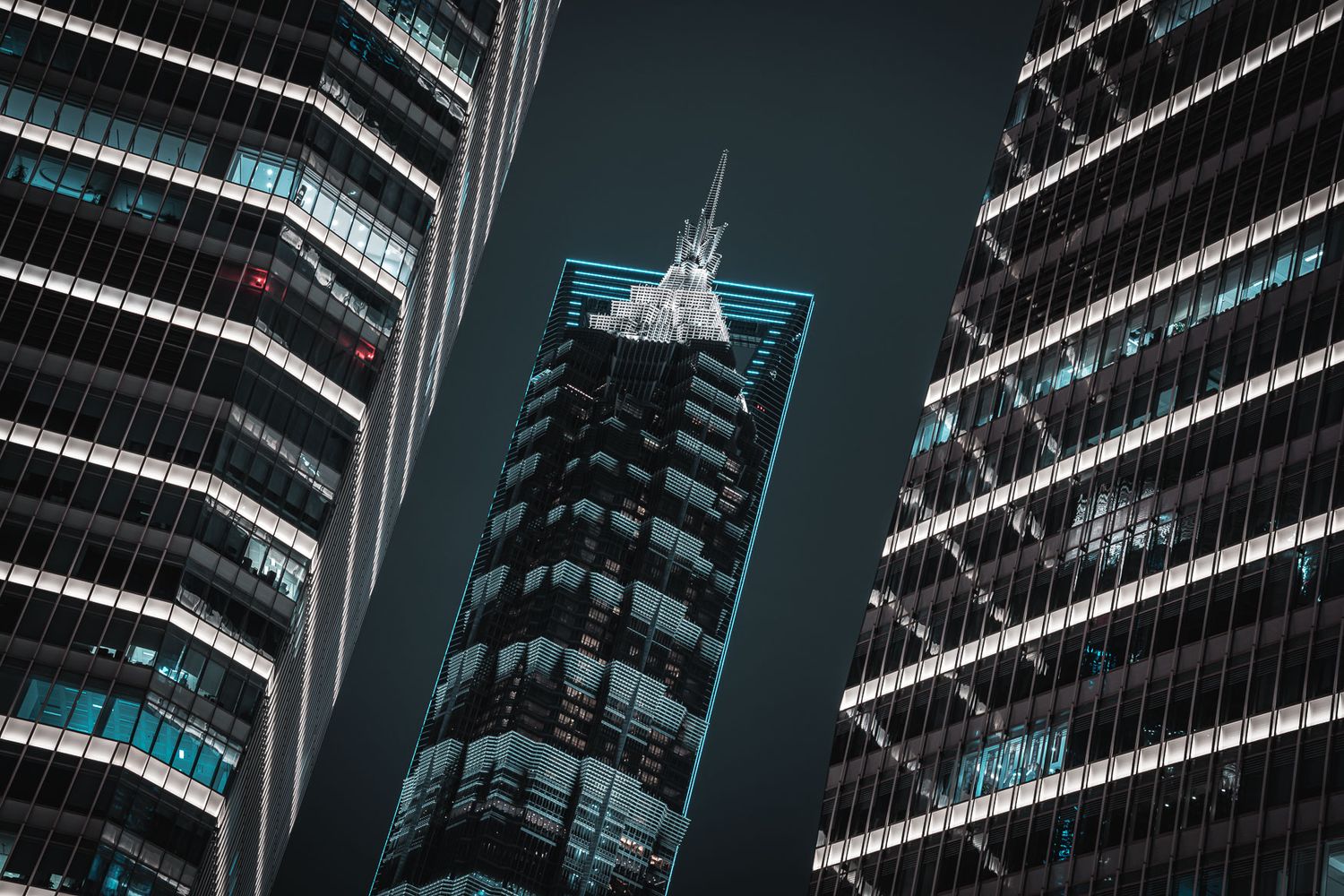 Towering skyscrapers frame a central building with blue accent lighting against dark sky.