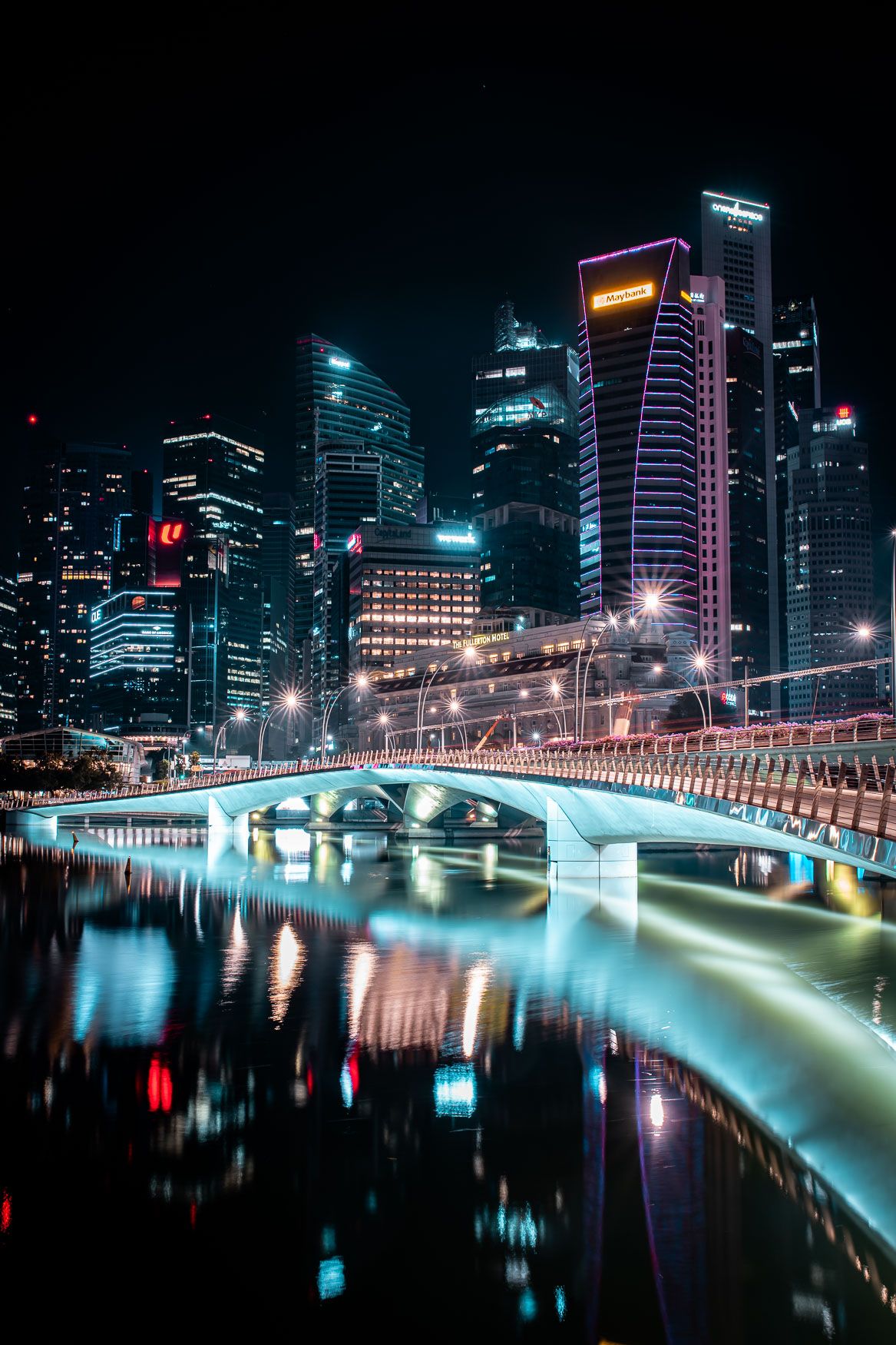 Modern cityscape with illuminated bridge reflecting in calm waters at night.