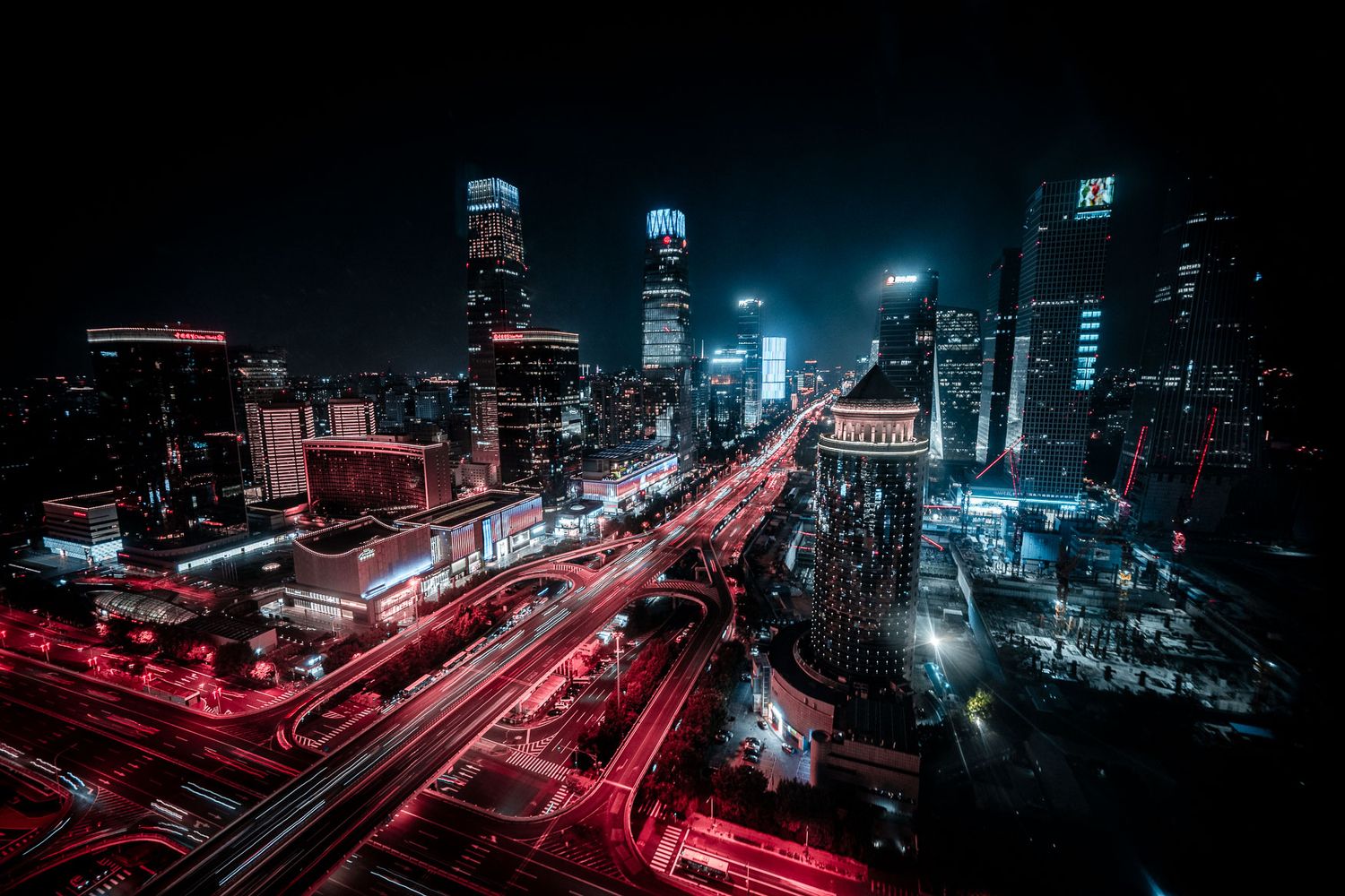 Aerial view of city streets with red light trails and glowing skyscrapers at night.