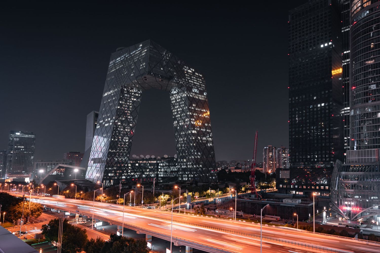 CCTV headquarters building illuminated at night with light trails from traffic below.