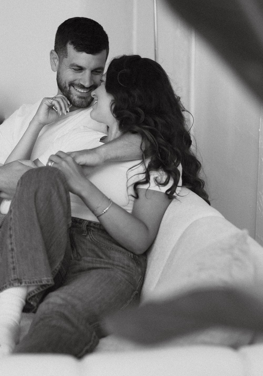 Black and white photo of a happy couple laughing and cuddling together on a couch indoors.