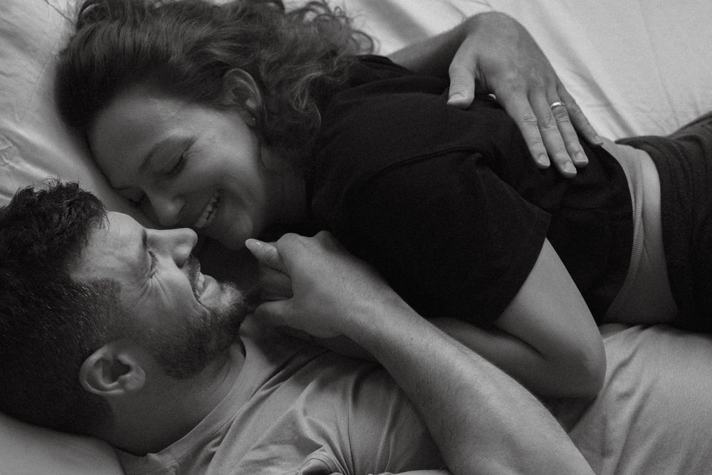 Black and white photo of a happy couple lying together on a bed, sharing a tender romantic moment.